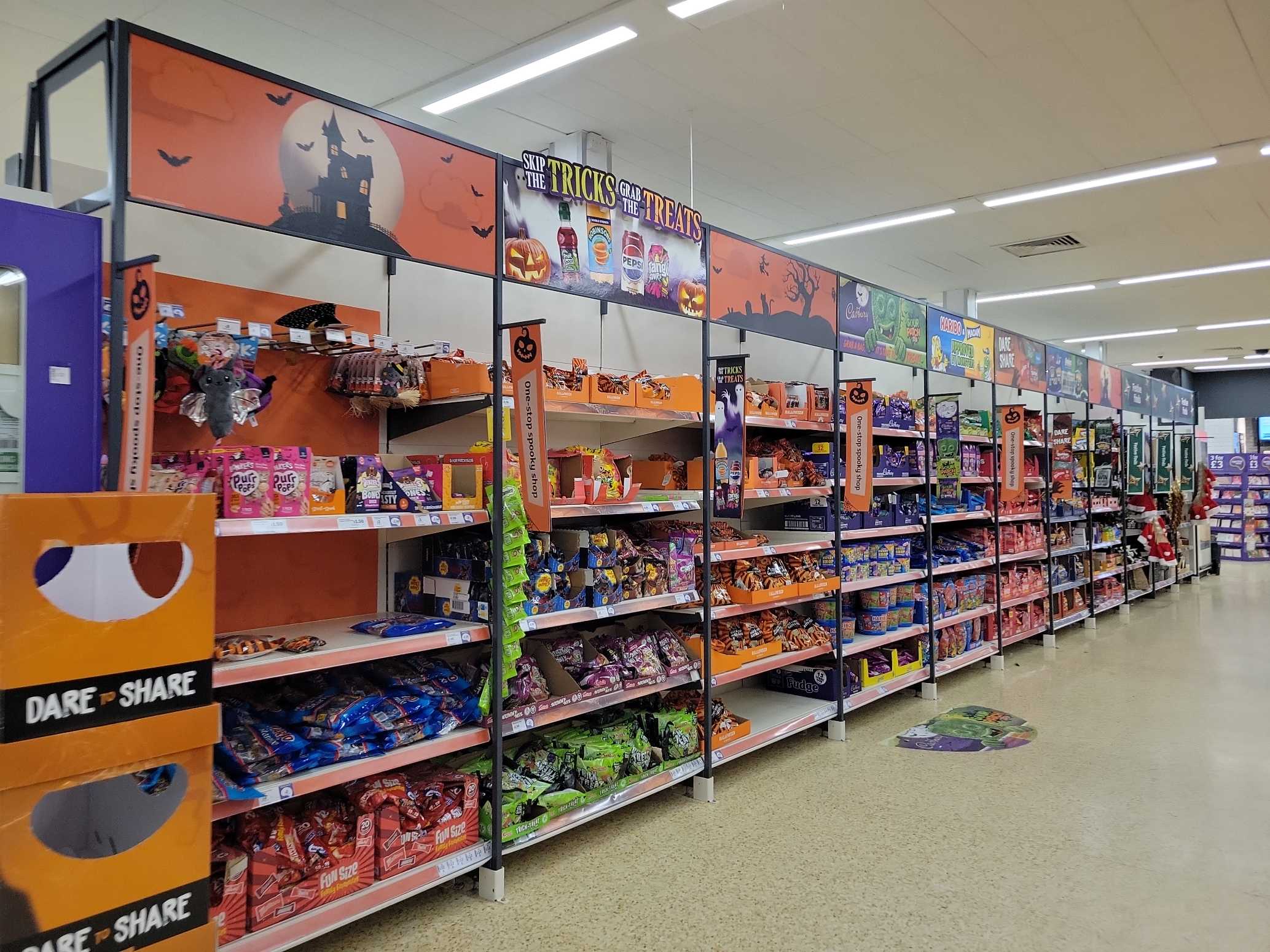 A long Halloween seasonal aisle in a UK supermarket, with Christmas products at the far end